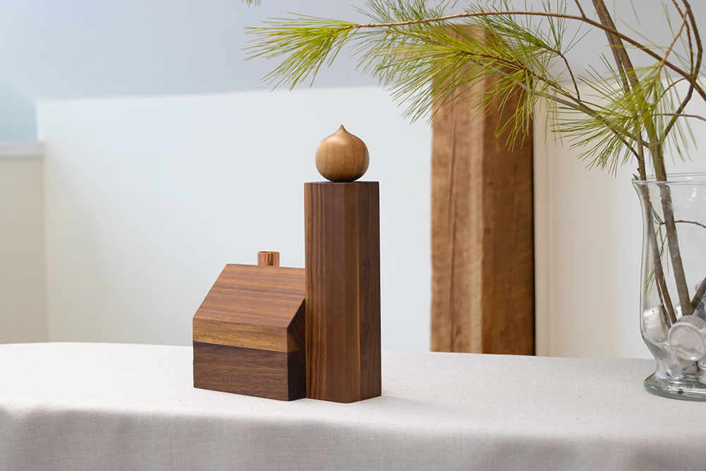 A wooden Alpine Church ornament with a hand-turned onion dome and a copper chimney sits on a linen-covered surface. Pine branches and a glass vase add a natural touch.