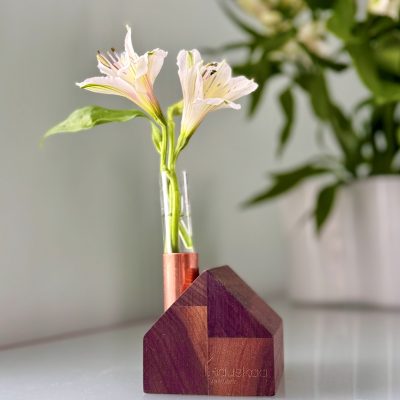 Farmhouse bud vase with pink flower on a green dresser with flowers in vase in the background