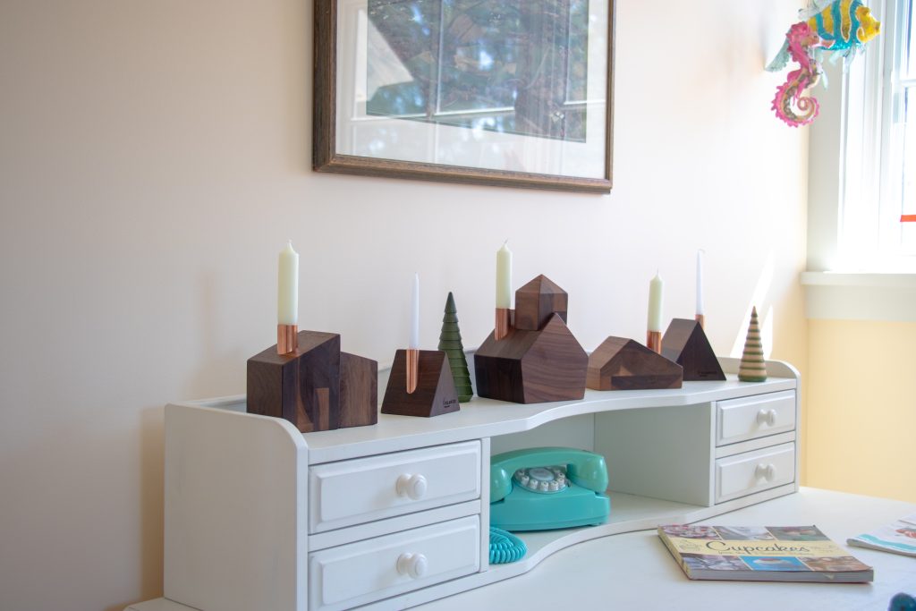 A set of wooden house candlestick holders on a white desk.