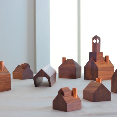 A tiny wooden village of candlestick holders in a white room.