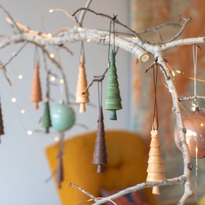 A decorative tree branch with little wooden Christmas tree ornaments, glass globes, and fairy lights draped across it.