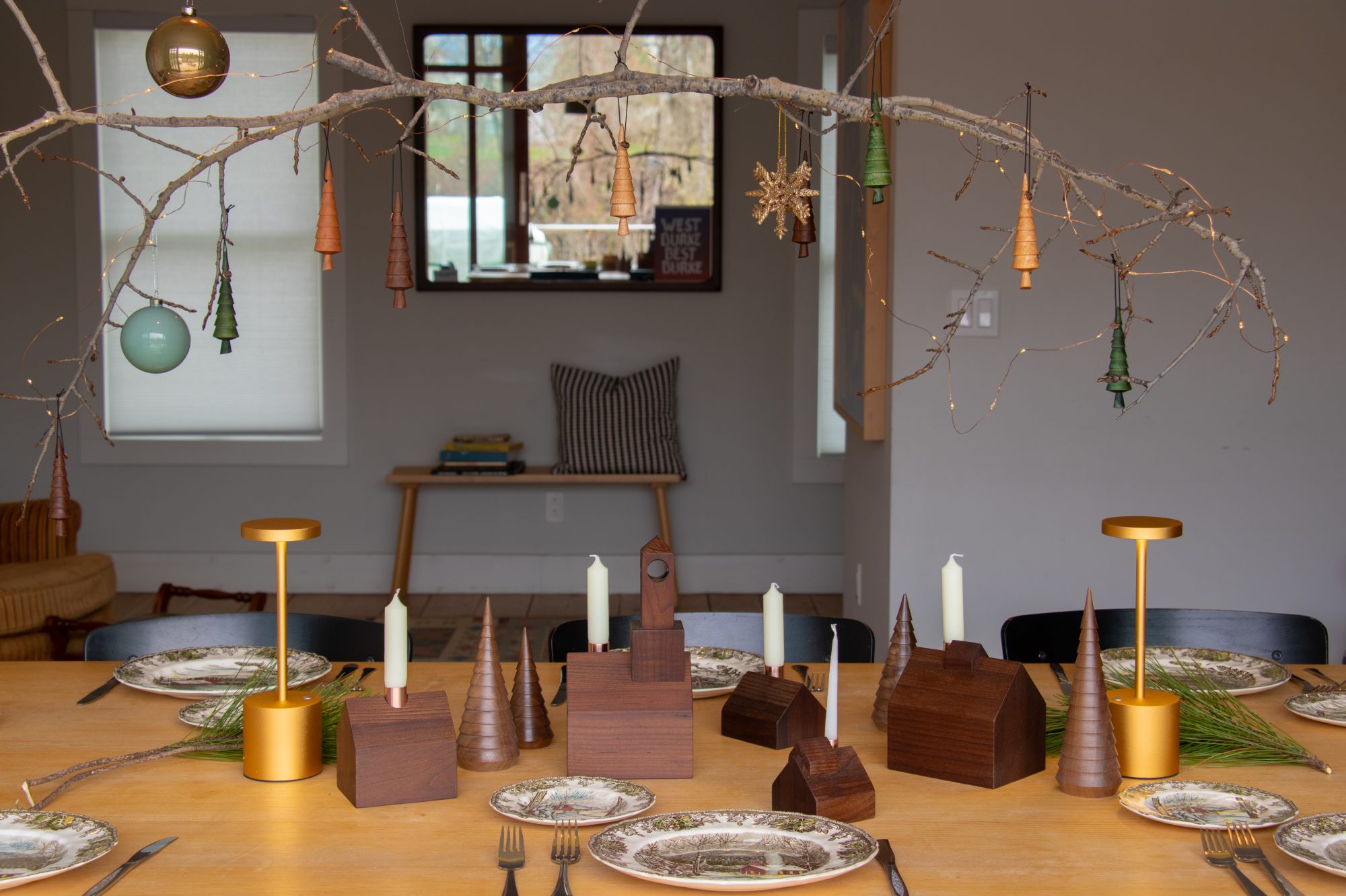 A wooden Christmas Village candlestick holder set decoratively displayed across a dinner table adorned with holiday-themed dinnerware.