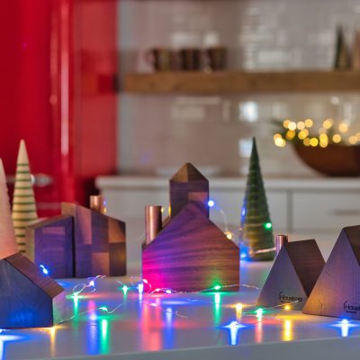 A retro Christmas village set of candlestick holders on a counter top surrounded by Christmas lights.