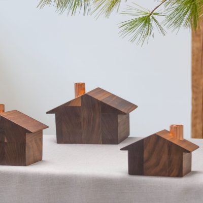 Small, medium and large chalets made from walnut wood with copper chimneys on top on a limen tablecloth with evergreen boughs overhead