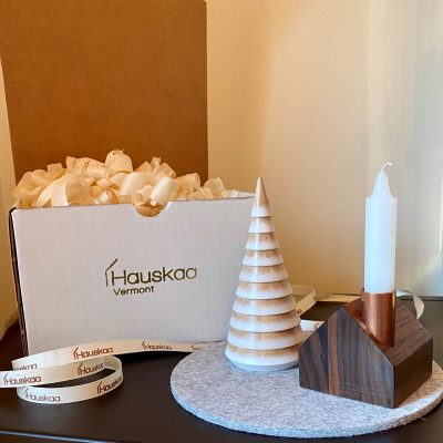 A tiny wooden house candlestick holder on a gray felt pad next to a tiny wooden tree and a box that says "Hauskaa, Vermont."